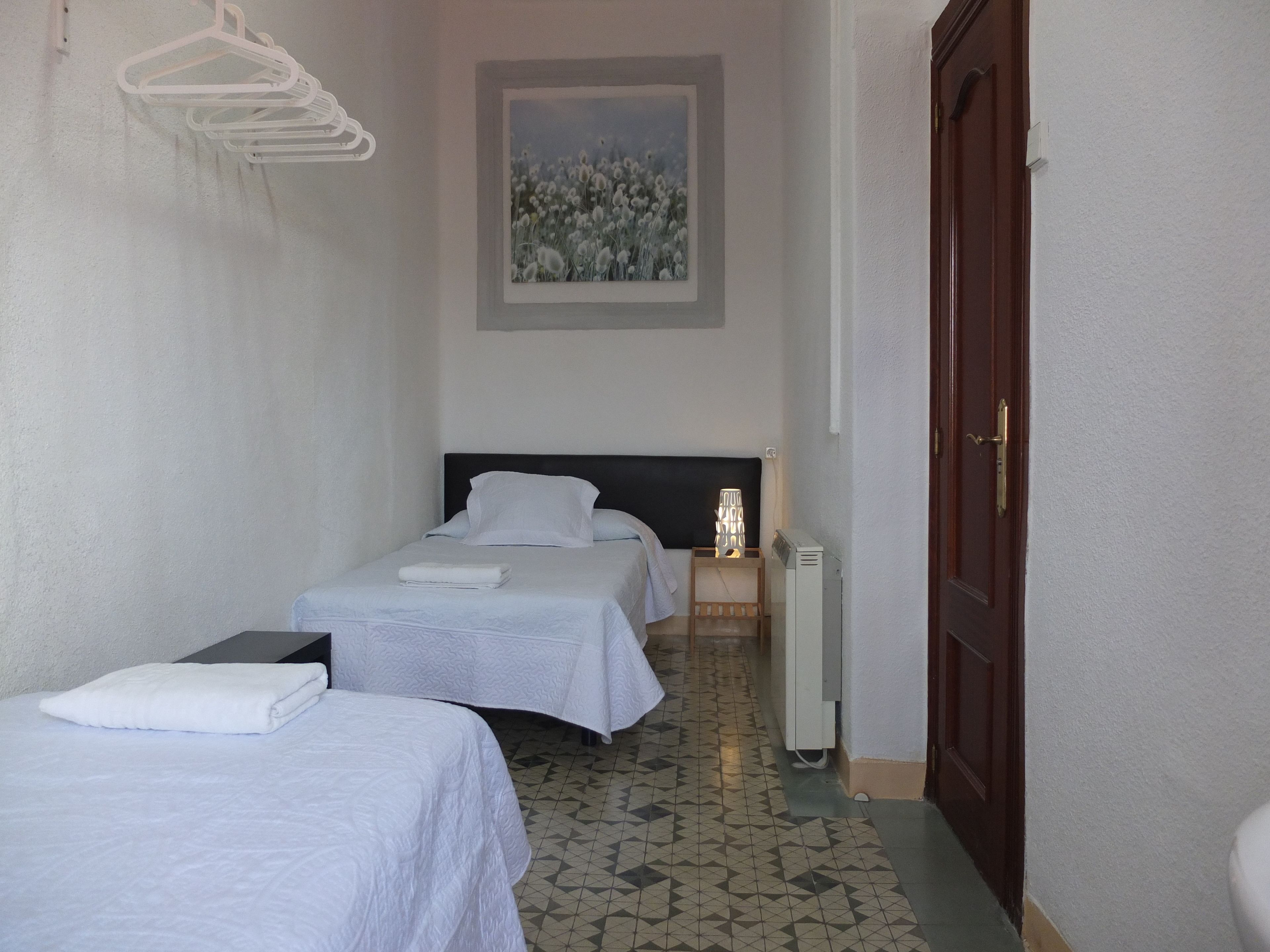 Una habitación de hotel con dos camas individuales, una mesita de noche con lámpara, un cuadro en la pared y una puerta.