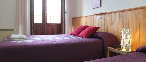 A hotel room with two beds, a wooden headboard, a nightstand with a lamp, and a window with curtains.