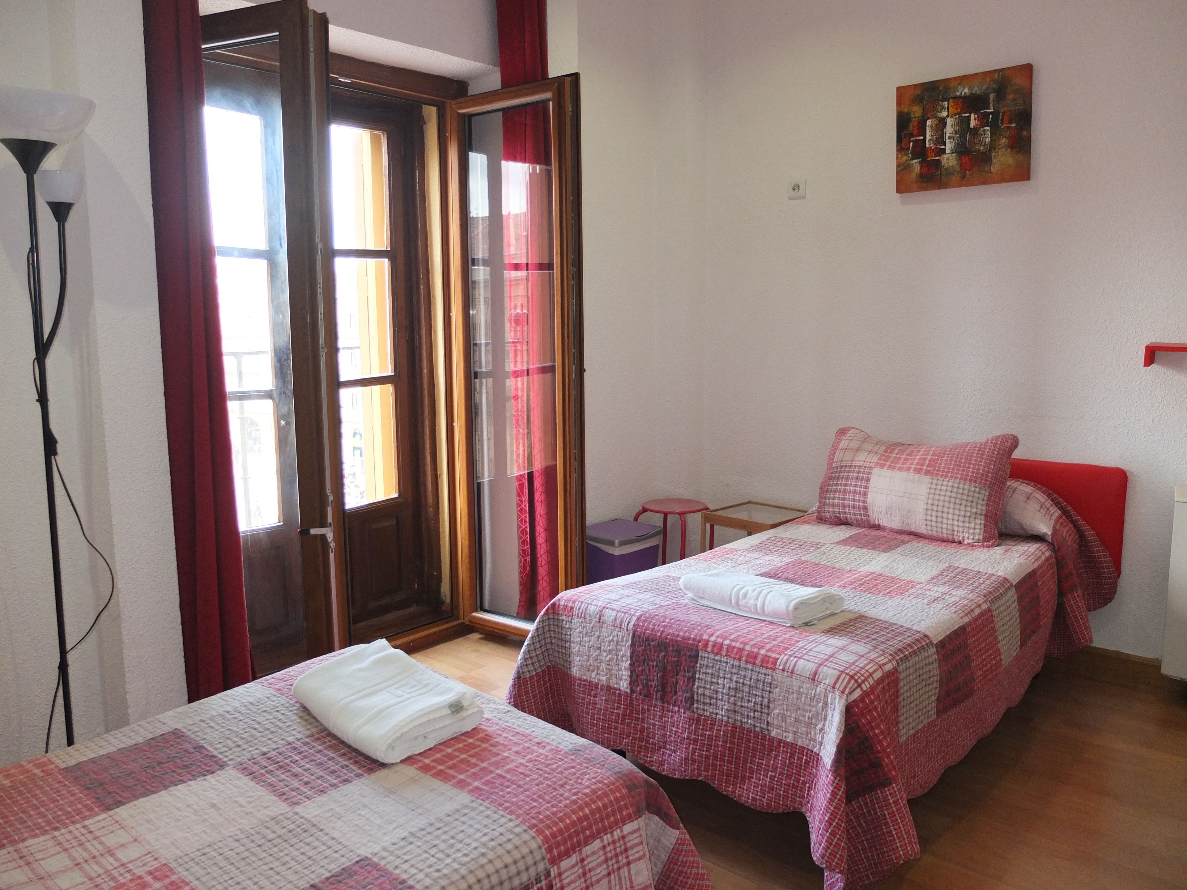 A bedroom with two beds, a red chair, a small table, and a painting on the wall.