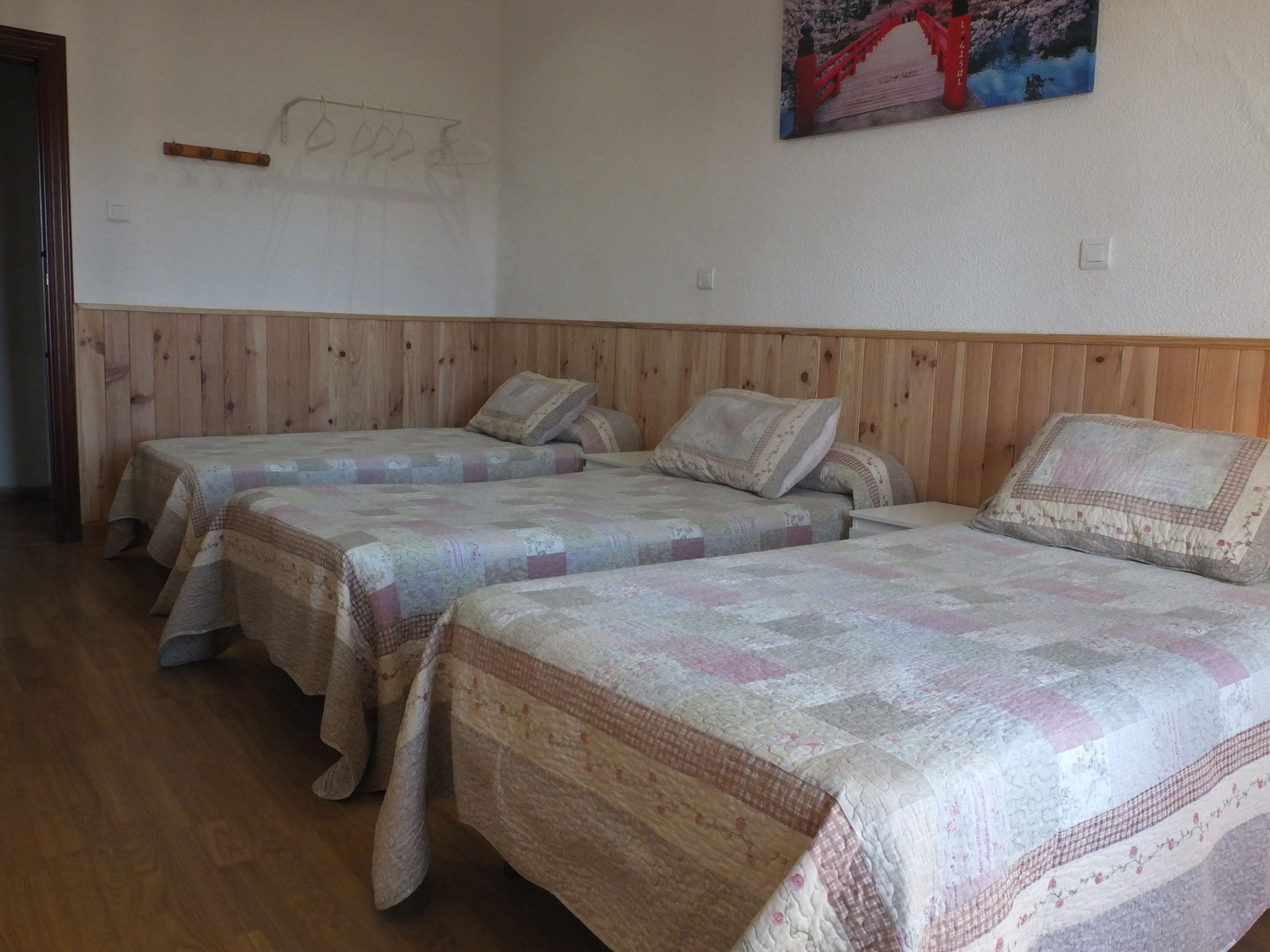 Une chambre avec trois lits, des murs recouverts de lambris en bois et un tableau représentant un pont.