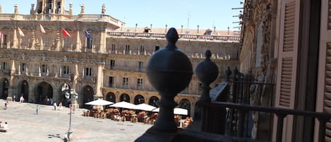 A courtyard with outdoor seating, a large ornate building with flags, and a clear sky.