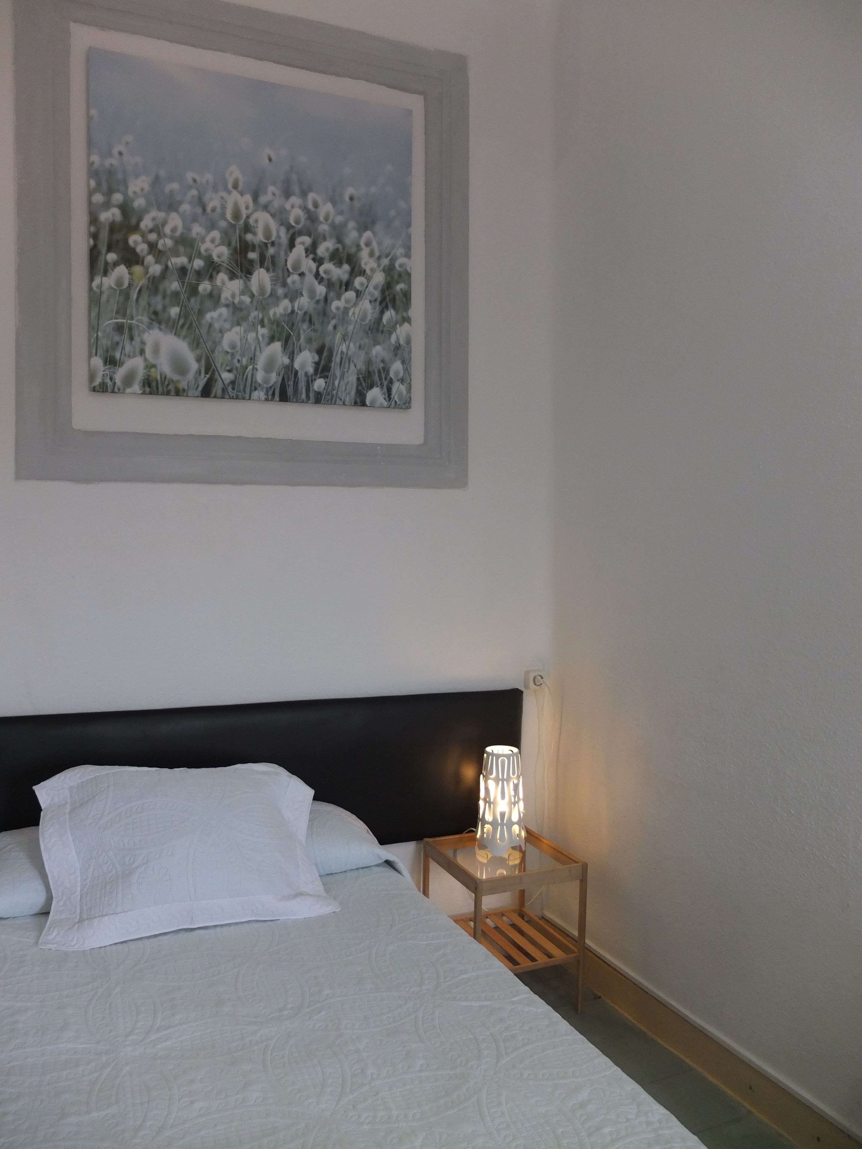 Un dormitorio con cama, mesita de noche, lámpara y un cuadro en la pared.