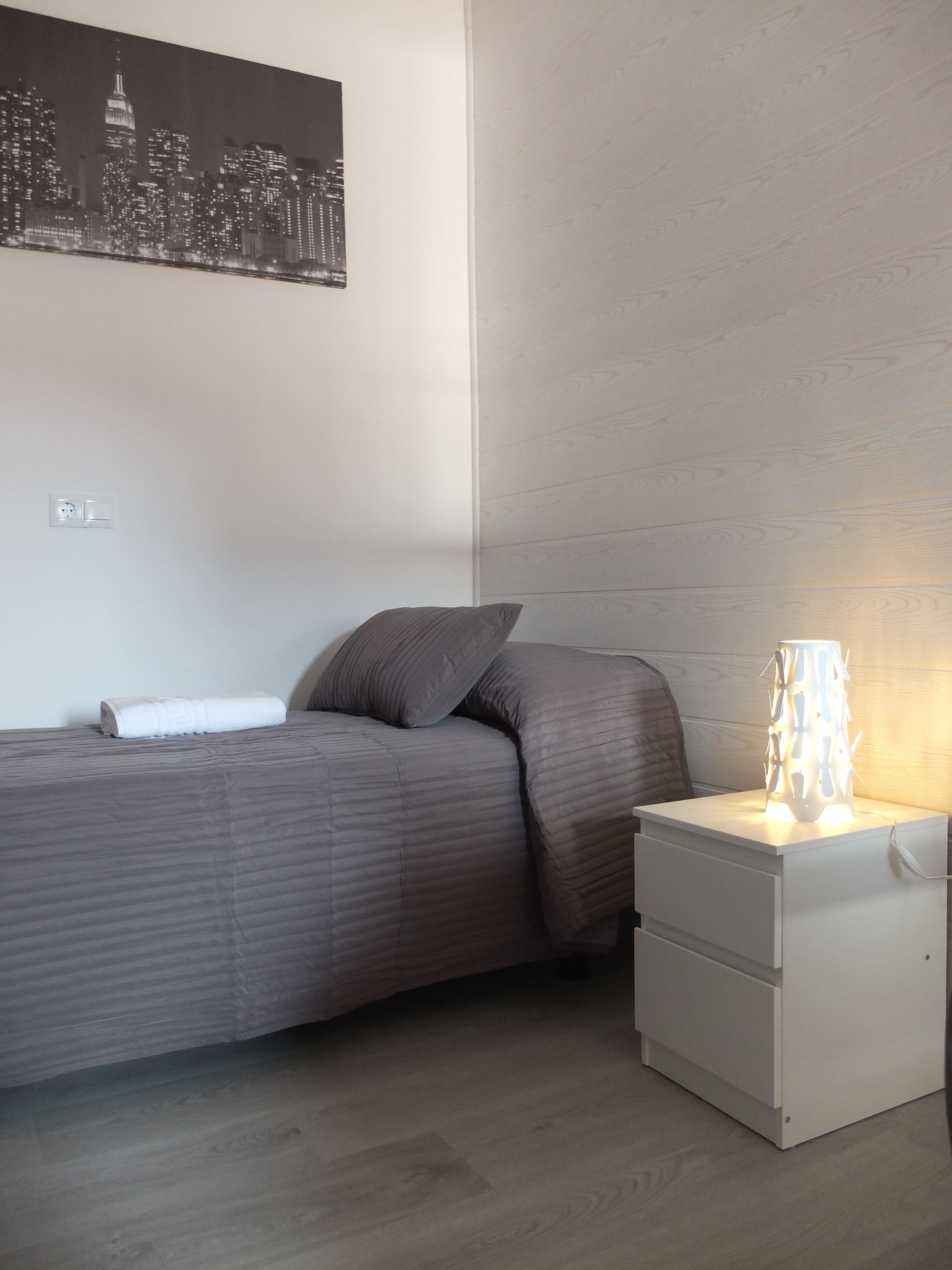 A bedroom with a bed, pillows, a nightstand, and a wall-mounted lamp.
