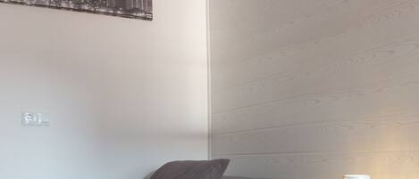 A bedroom with a bed, pillows, a nightstand, and a wall-mounted lamp.