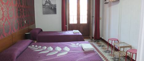 A hotel room with two beds, a red curtain, a wall-mounted TV, and a patterned floor.