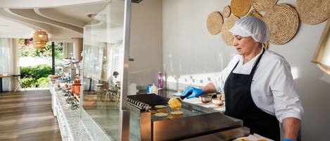 A person cooking pancakes on a griddle in a modern kitchen with a glass partition.