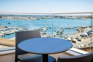 A balcony with a view of a marina, a round table, and two chairs.