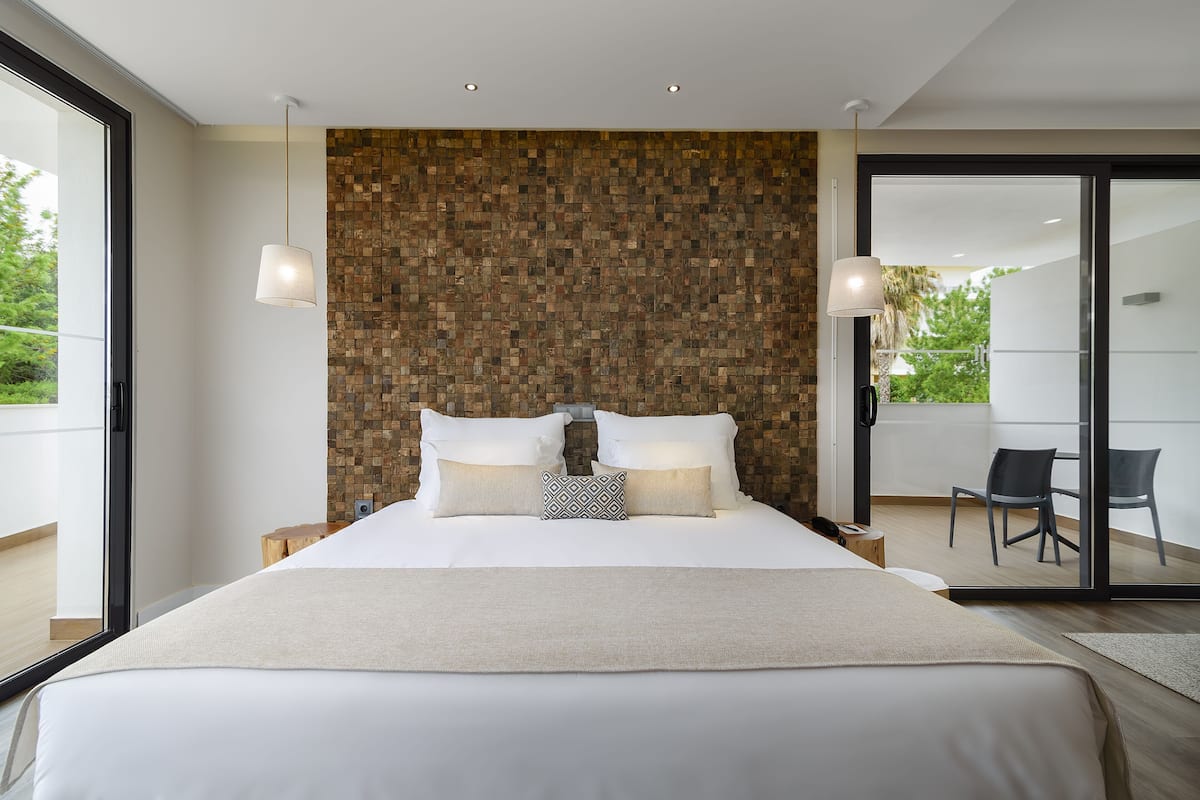 A modern bedroom with a large bed, a wooden mosaic wall, and a balcony with chairs.