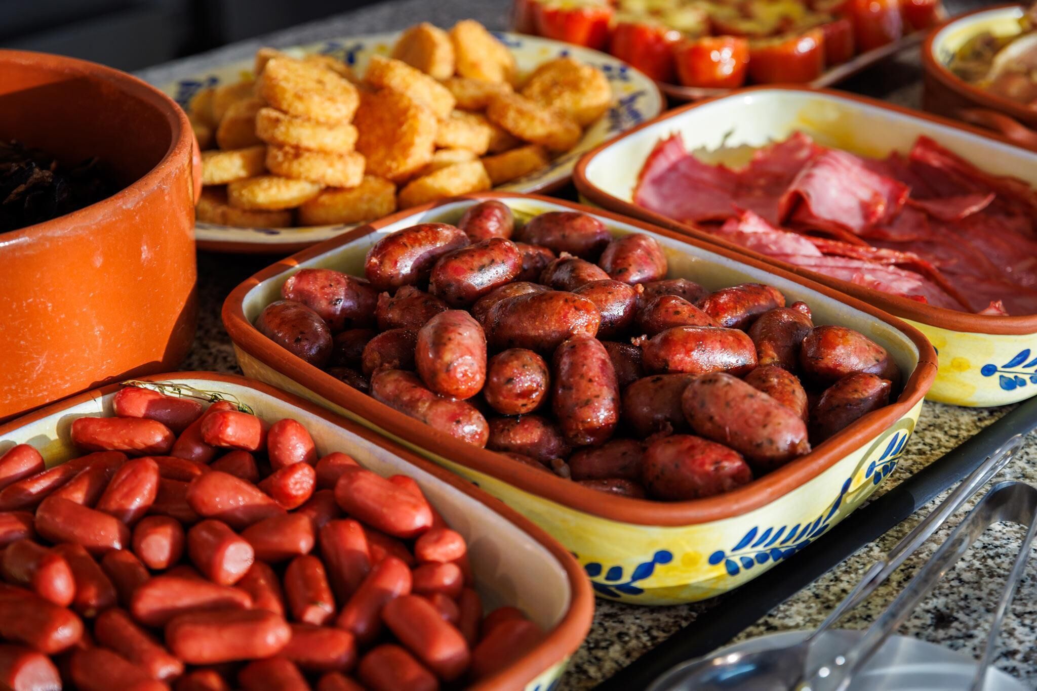 Diverse gerechten, waaronder worst, brood en ham, op een tafel.