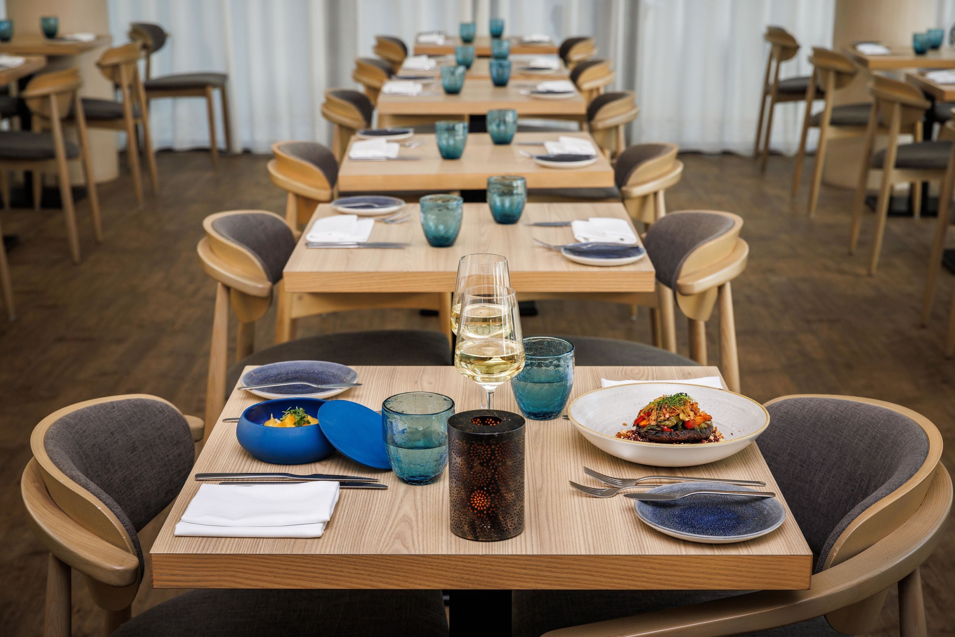 Un espace repas avec plusieurs tables dressées pour les repas, chacune étant équipée d’assiettes, de bols, de verres et de couverts.