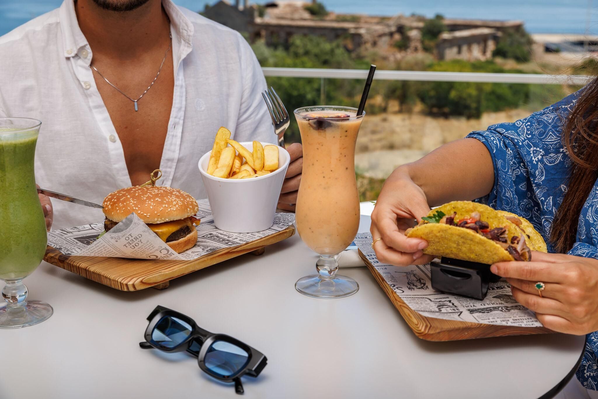 A table with a burger, fries, a drink, and a taco, with a scenic view in the background.