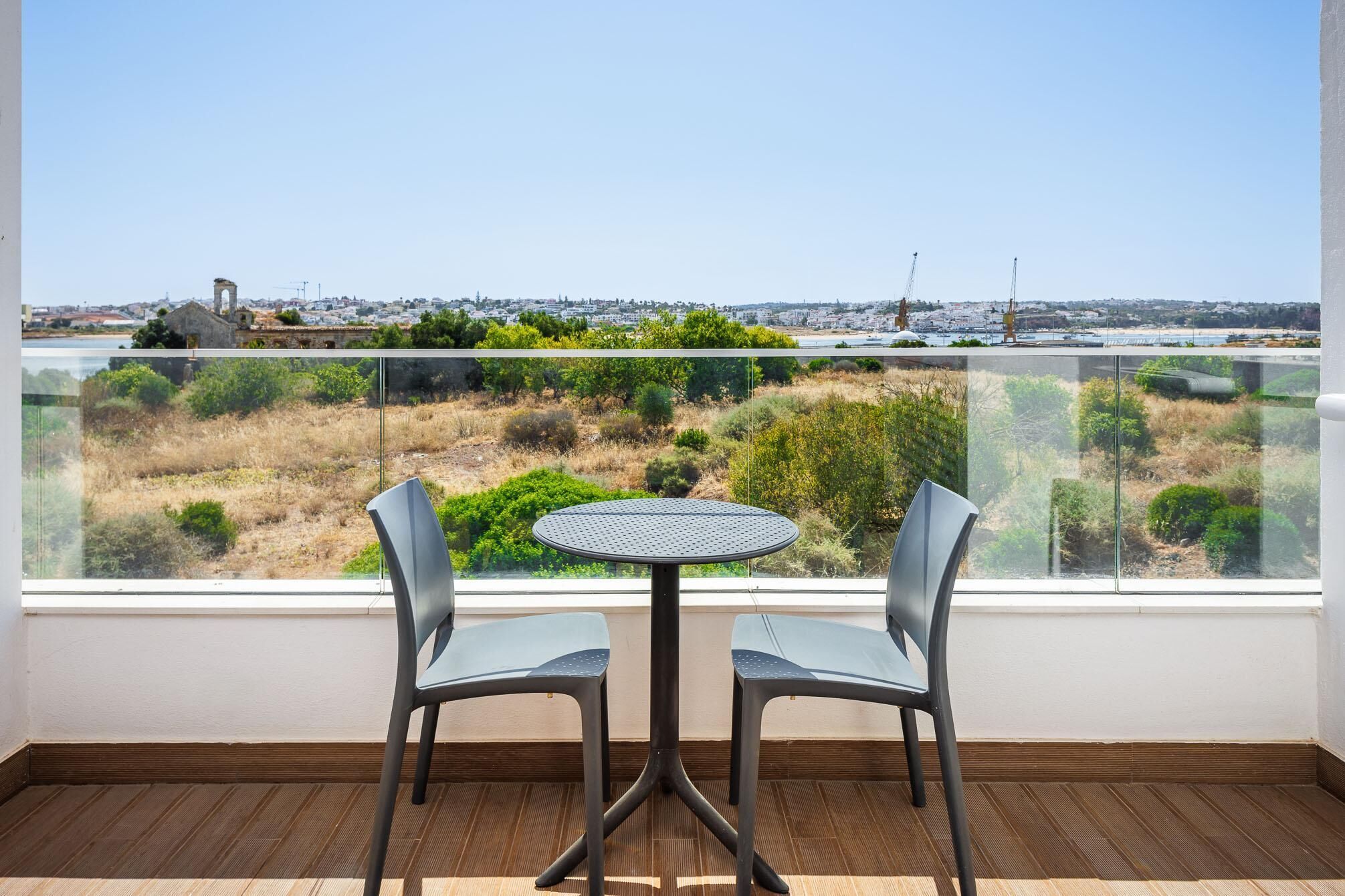 Un balcón con una mesa redonda y dos sillas, con vista a un paisaje urbano y un área verde.