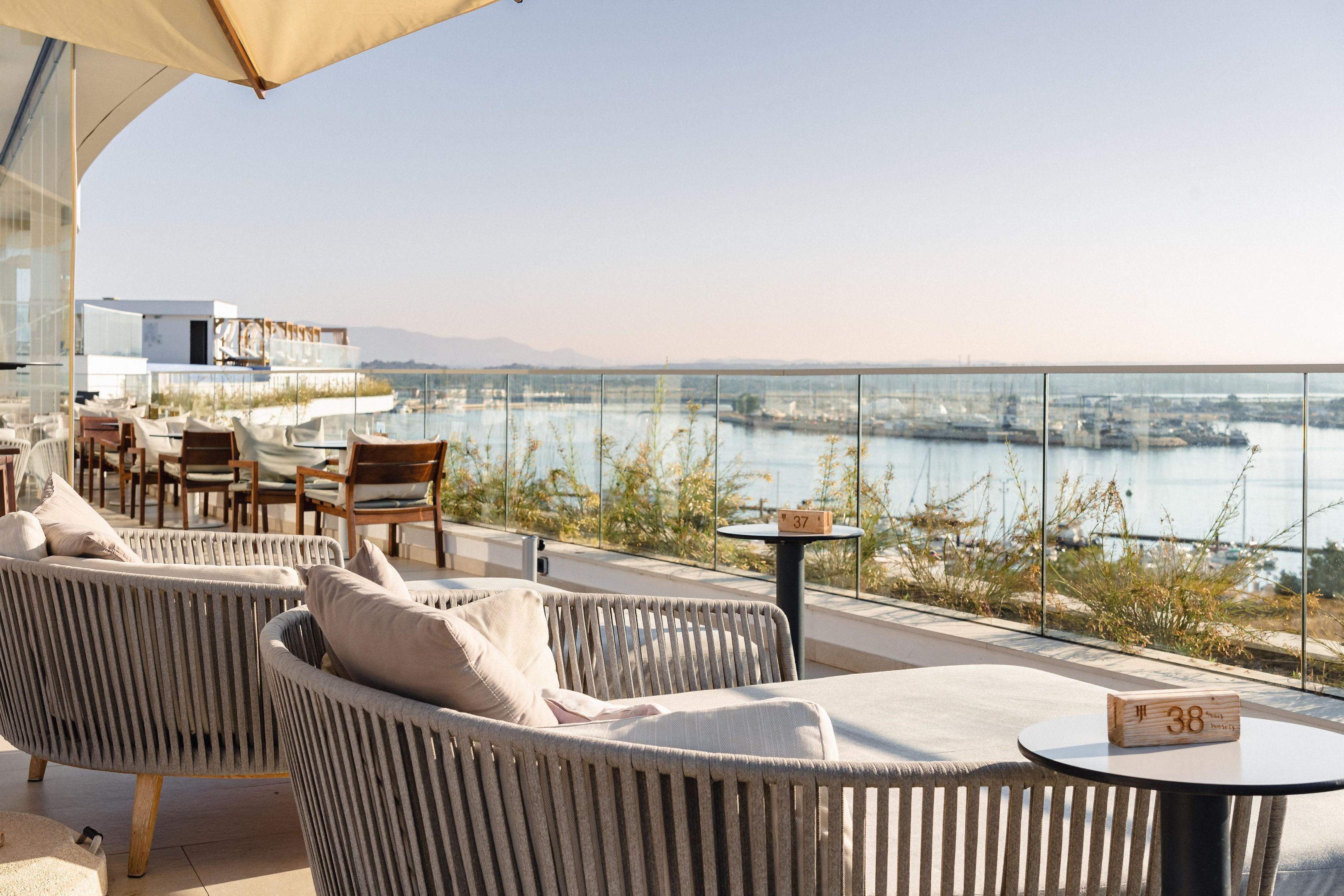 A terrace with wicker furniture, a table with a block number, and a view of a body of water and cityscape.