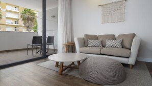 Ein modernes Wohnzimmer mit einer Couch, zwei Sesseln, einem runden Couchtisch und einer Wanddeko aus Makramee.