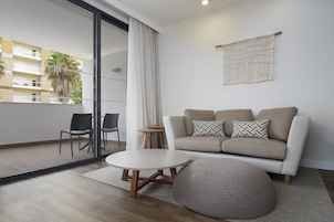 A modern living room with a sofa, two chairs, a round coffee table, and a macrame wall hanging.