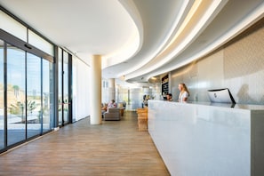 A modern hotel lobby with a reception desk, seating area, and large windows offering a view of the outdoors. - Jupiter Marina Hotel - Couples & Spa (Portimão)
