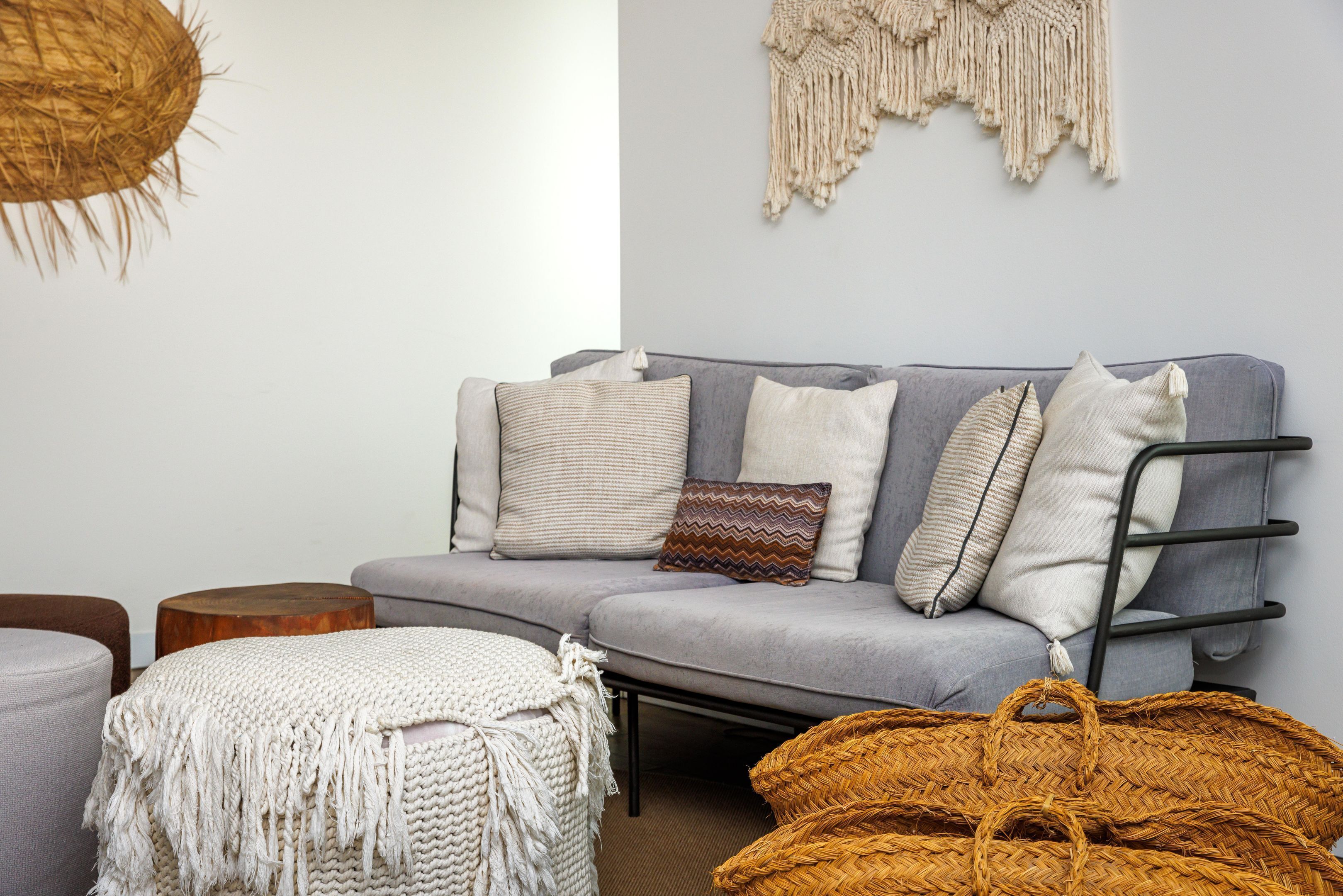 A modern living room with a grey sofa, multiple cushions, a woven basket, and a macrame wall hanging.