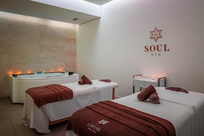 A spa room with two beds, a bathtub, and a wall-mounted logo.