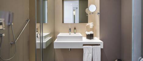 Un baño moderno con cabina de ducha de vidrio, lavamanos blanco, espejo y toallero.
