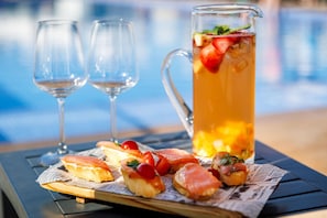 A table with a pitcher of iced tea, glasses, and small sandwiches on newspaper.