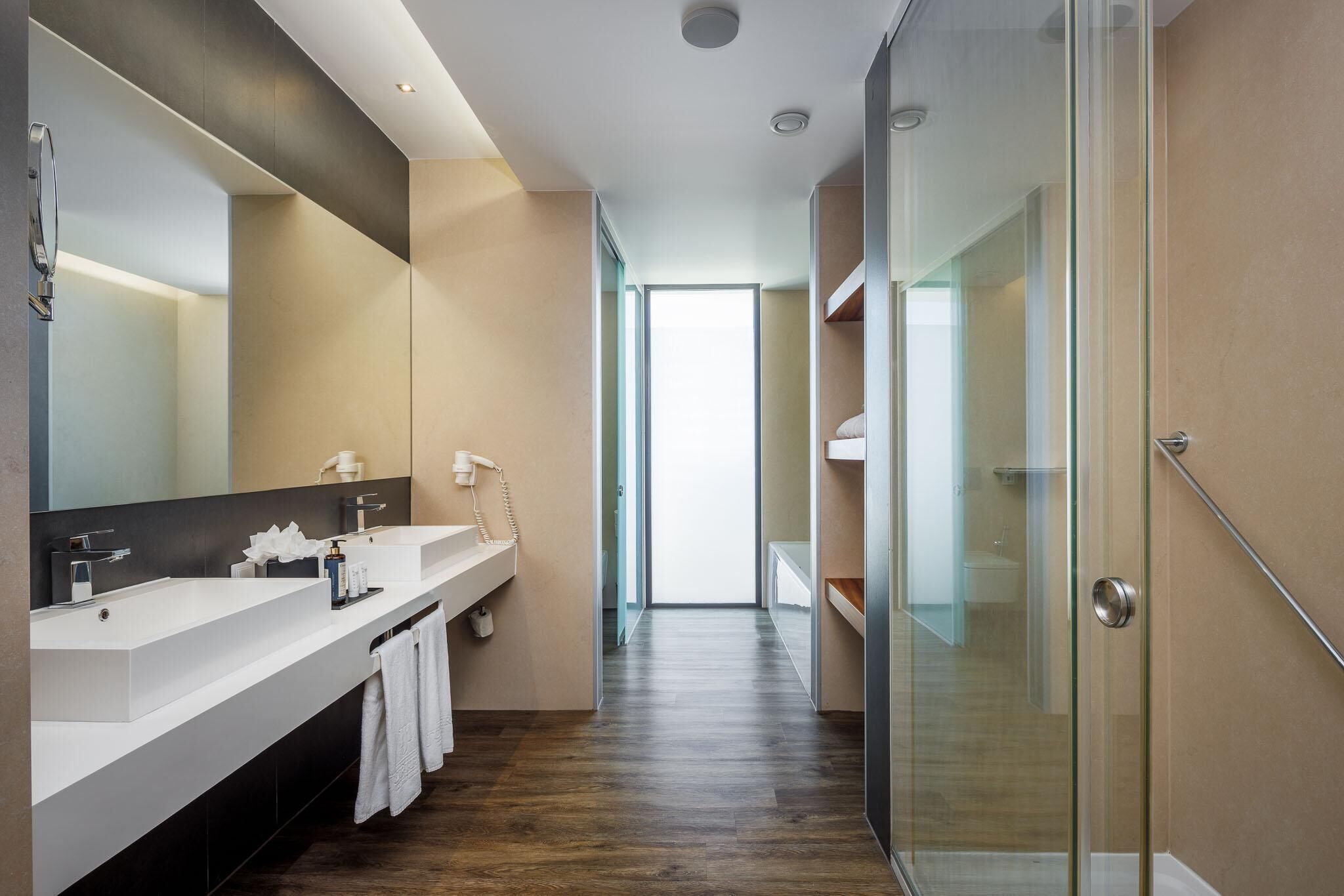 A modern bathroom with a large mirror, two sinks, and a glass shower enclosure.