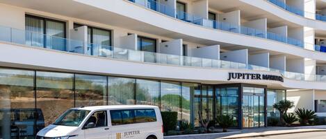 Una camioneta blanca estacionada frente a un hotel moderno con varios balcones y una vista despejada del paisaje circundante.