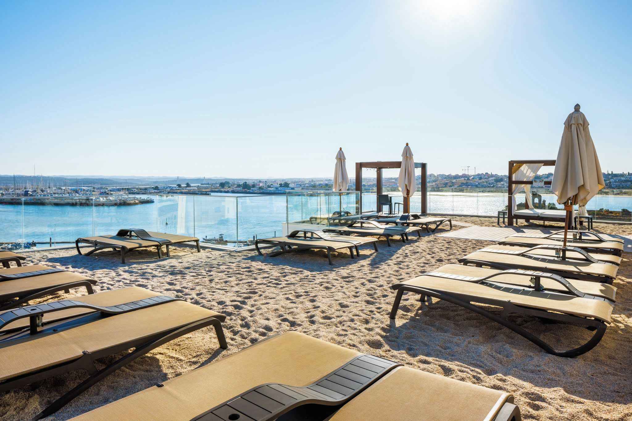 A beachside lounge area with sun loungers, umbrellas, and a view of the water.