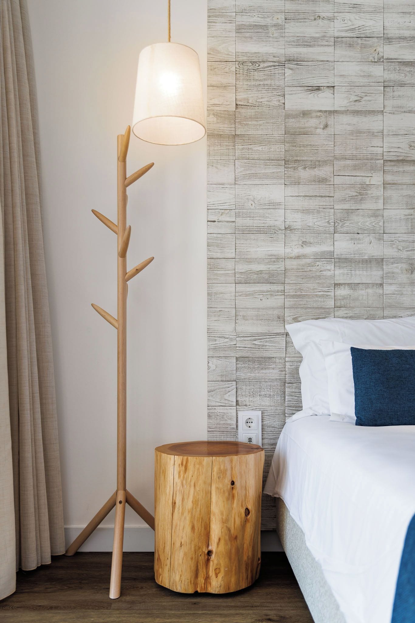 Un dormitorio con una cama, una mesita de noche, una lámpara y una pared con diseño que simula madera.
