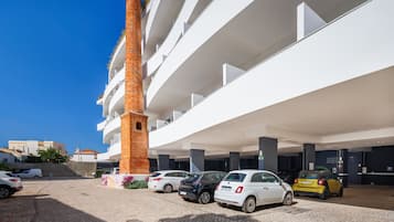 Um edifício moderno com vários andares, uma área de estacionamento com diversos carros e um colunar de tijolos imponente.