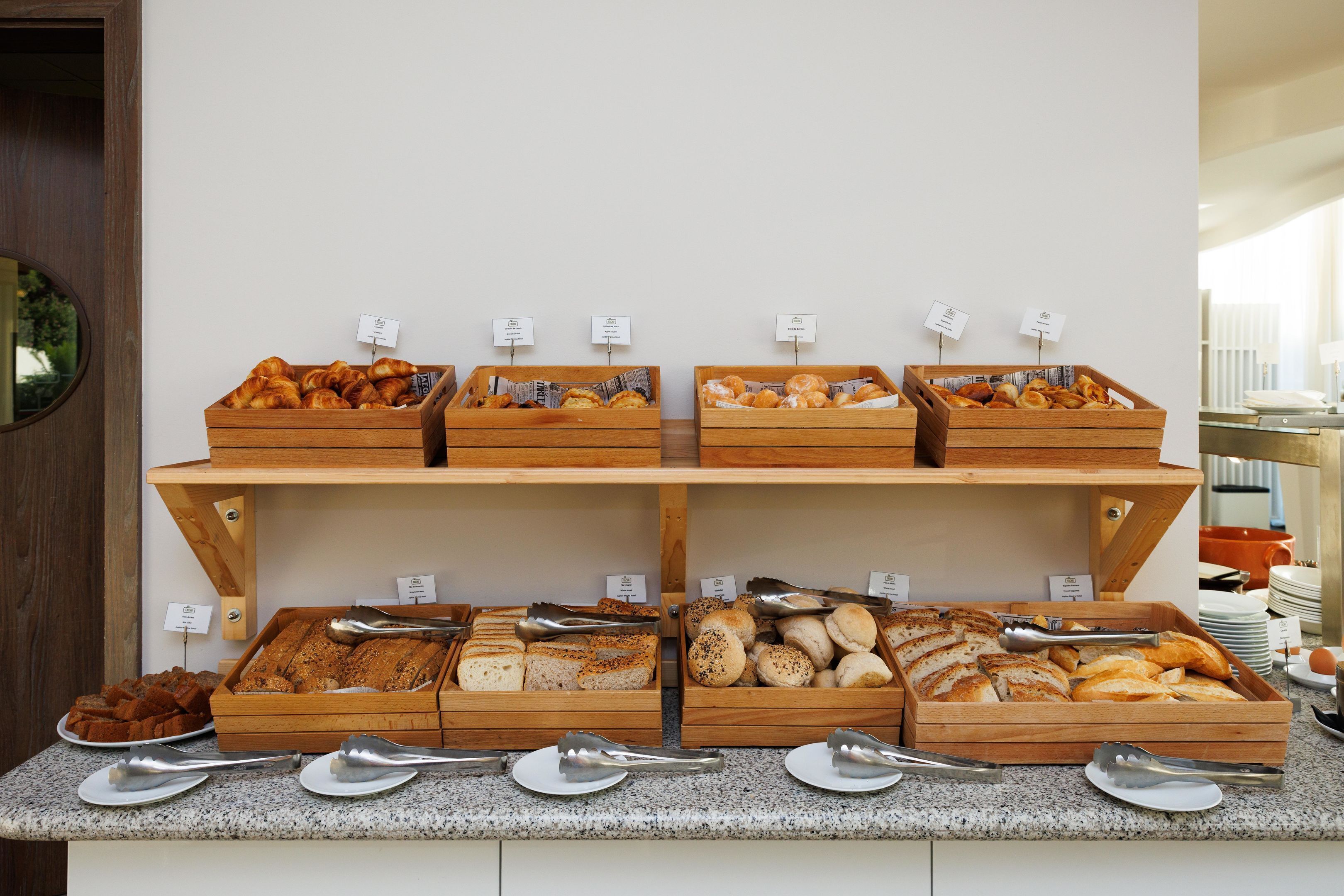 Een buffet met diverse gebakjes en brood, gepresenteerd op houten schalen, met bestek en prijslabels.