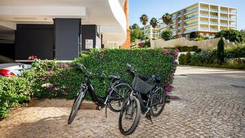 Una bicicleta estacionada frente a un edificio de diseño moderno, un área pavimentada y una estructura de varios pisos al fondo.