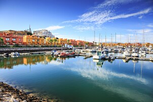 Un puerto deportivo con barcos amarrados, cielo despejado y edificios coloridos al fondo.