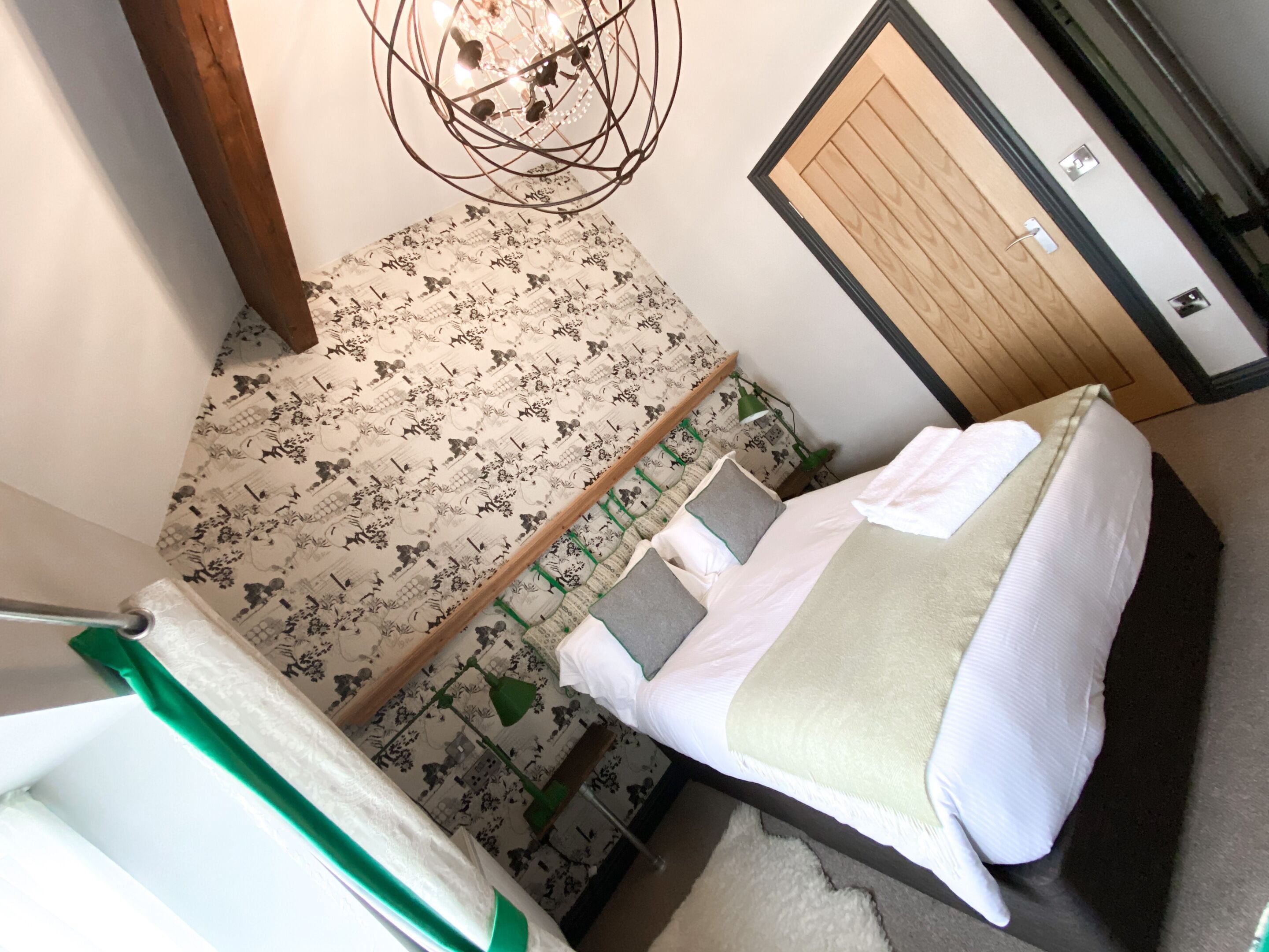 Un dormitorio con una cama, una silla verde, una puerta de madera y un suelo con estampado.