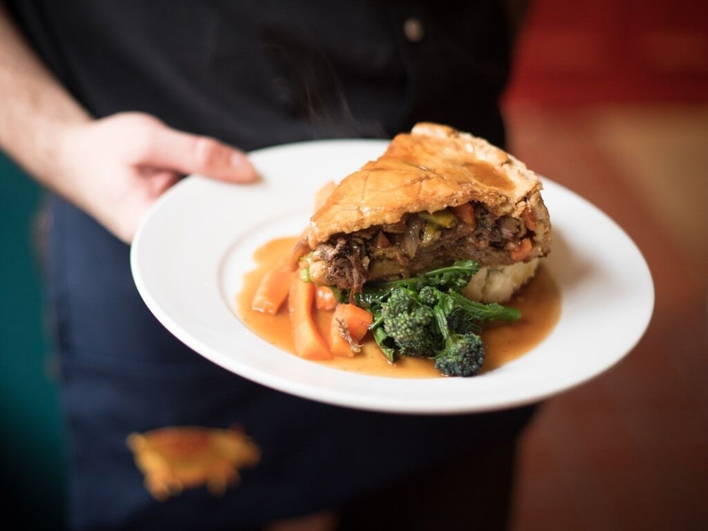 A person holding a plate with a meat dish, vegetables, and sauce.