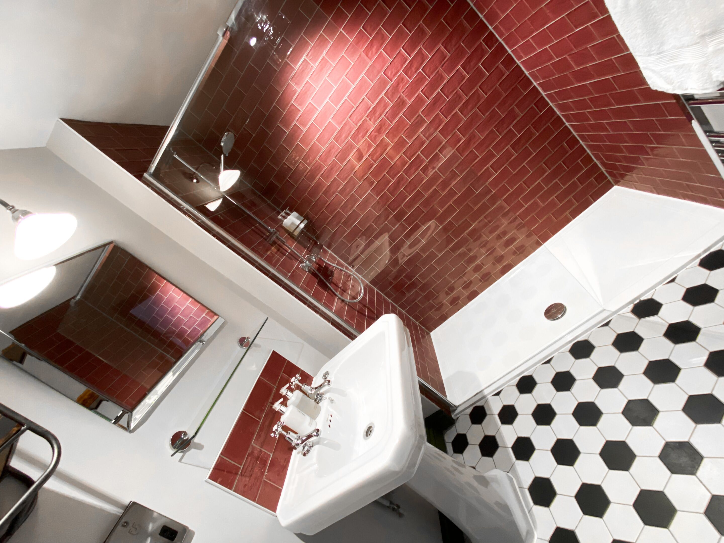 A modern bathroom with a red-tiled shower wall, a white sink, and a black-and-white hexagonal tile floor.
