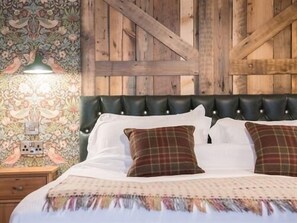 A bedroom with a tufted headboard, a patterned wallpaper, and a wooden wall. - Helen Browning's Royal Oak (Swindon)