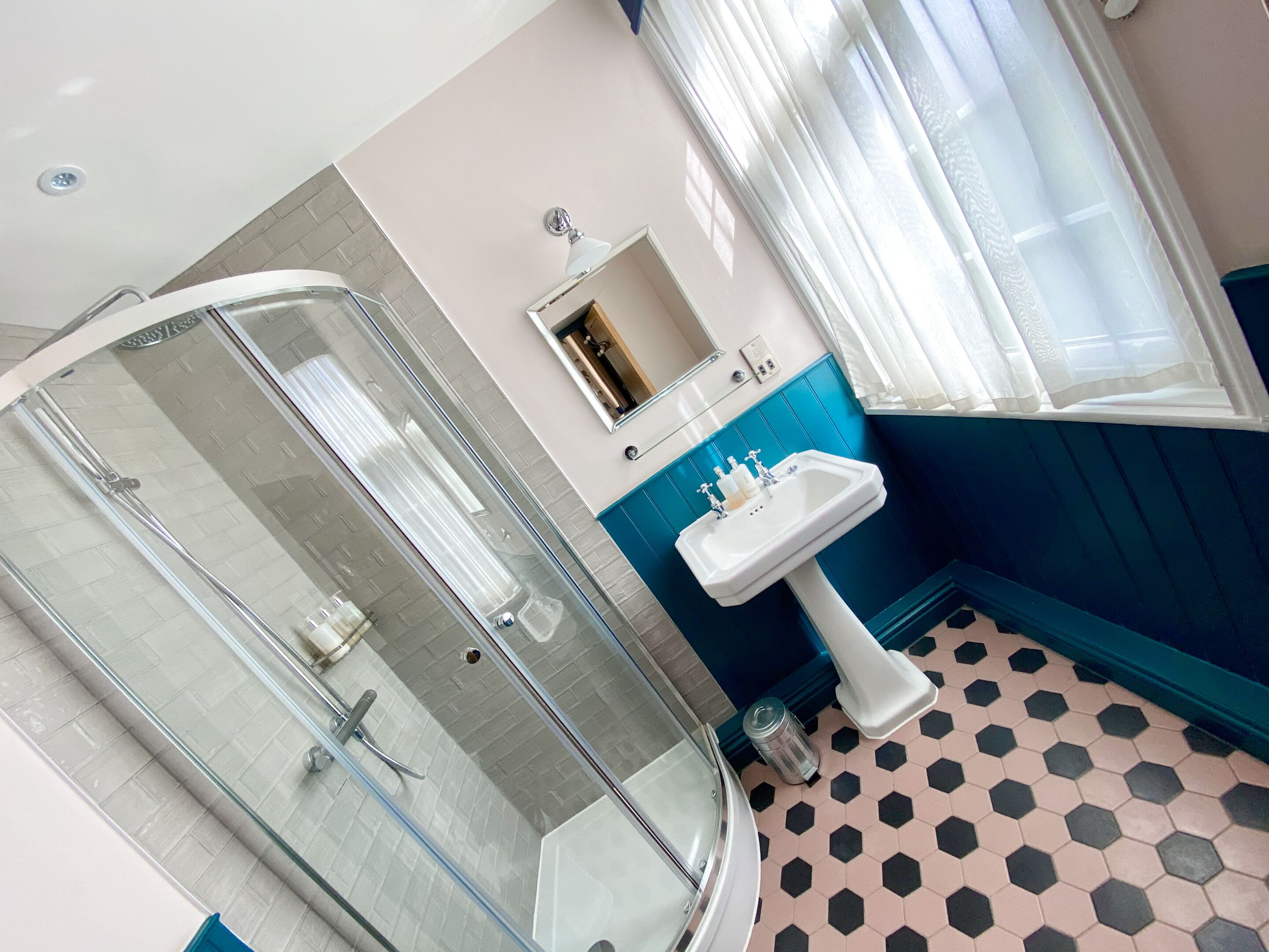 A bathroom with a glass-enclosed shower, a sink with a mirror above it, and a window with curtains.