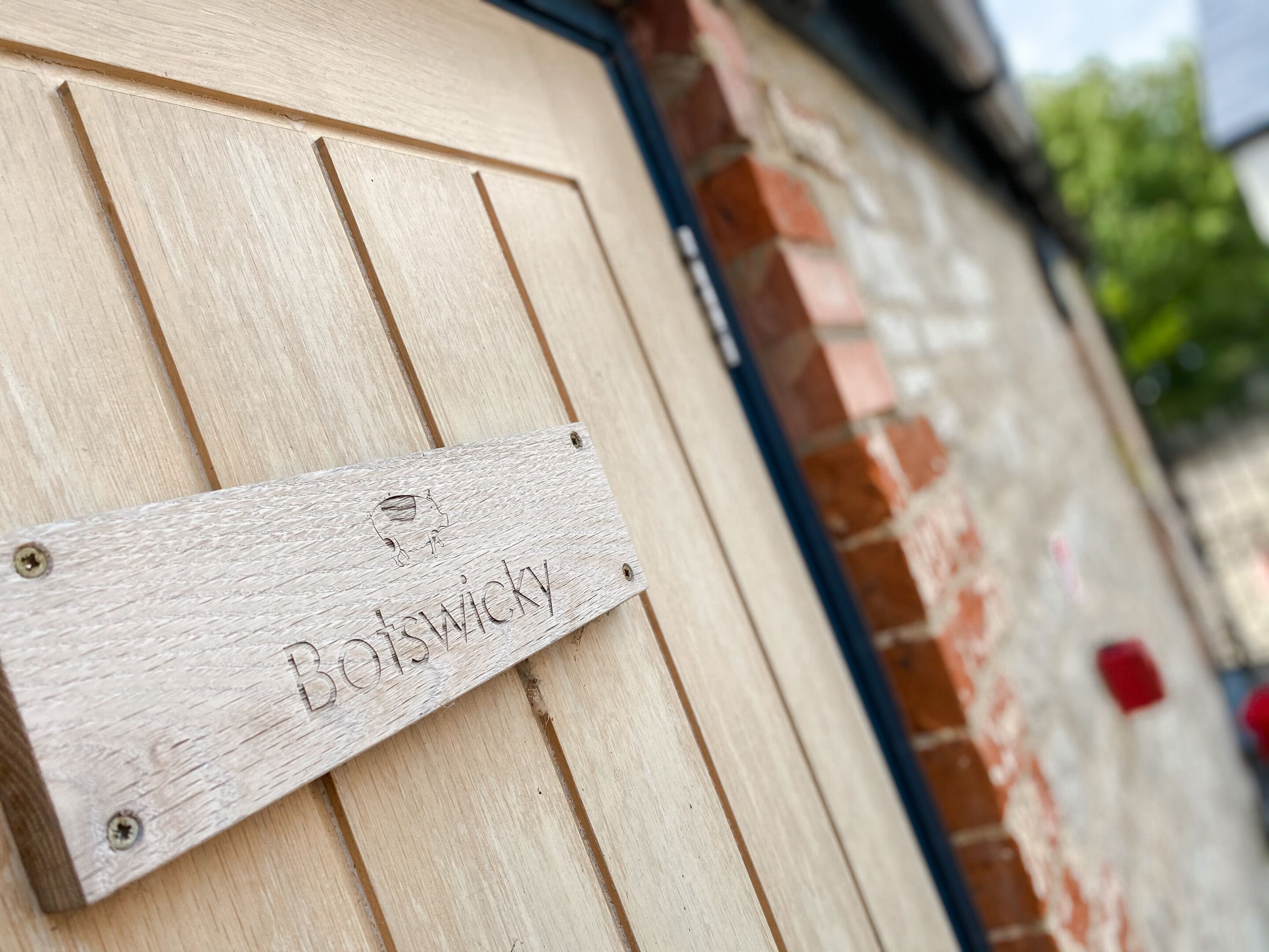 A wooden sign with the name "Bowsherwick" mounted on a building with a brick facade.