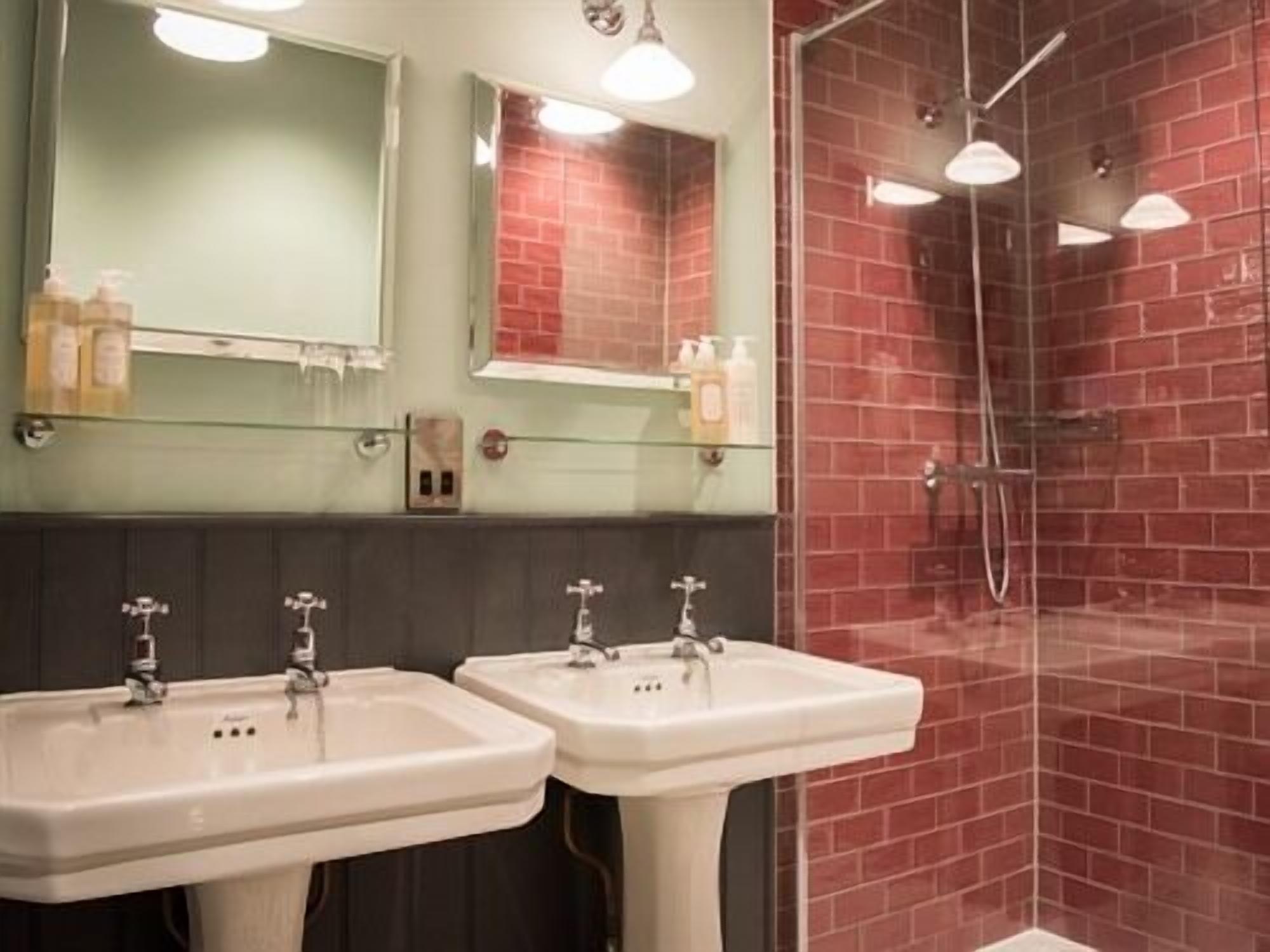 A bathroom with two sinks, a mirror, and a shower area with red tiles.