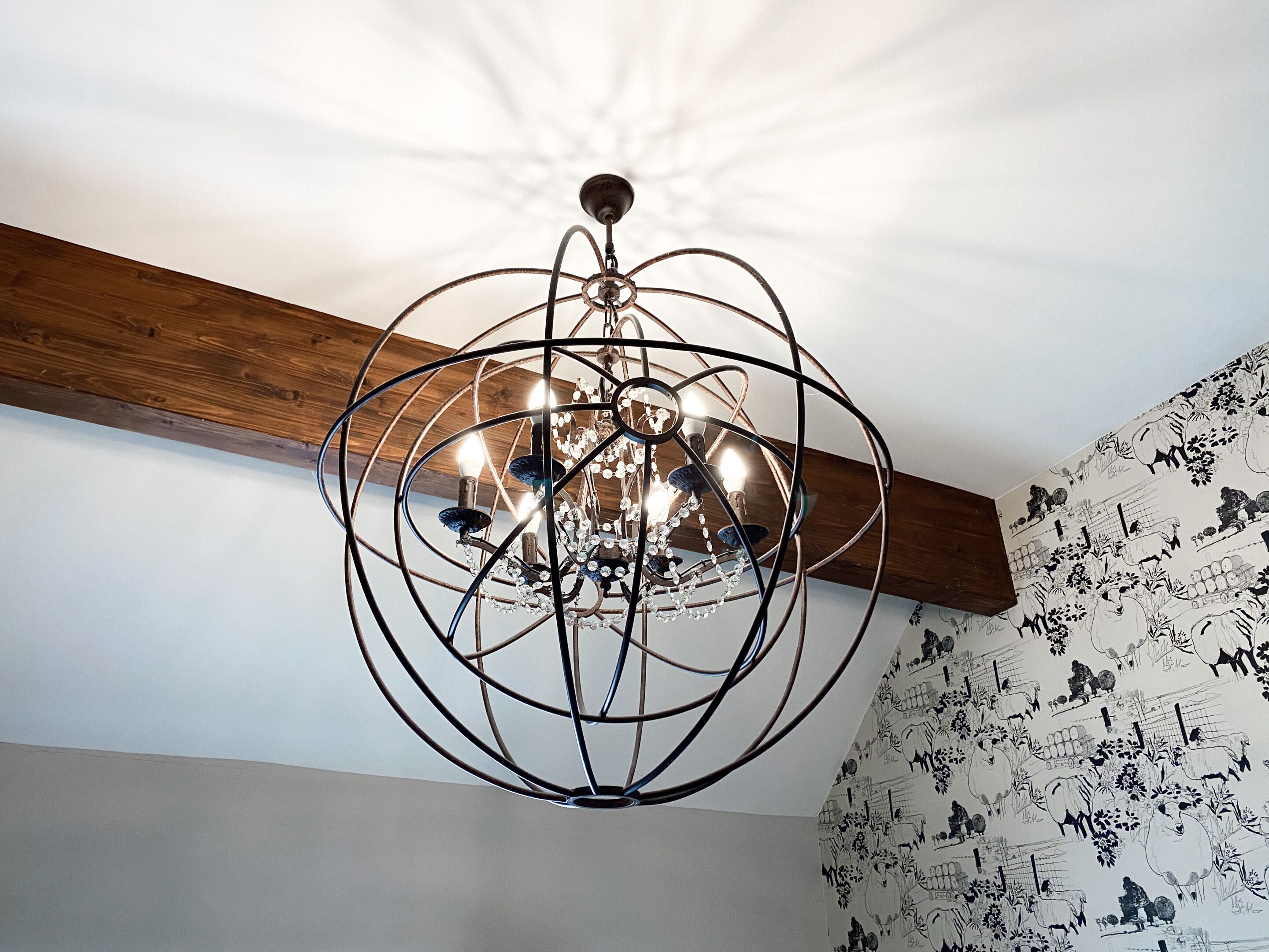 Un lustre au design géométrique, doté de plusieurs ampoules, fixé à une poutre en bois.