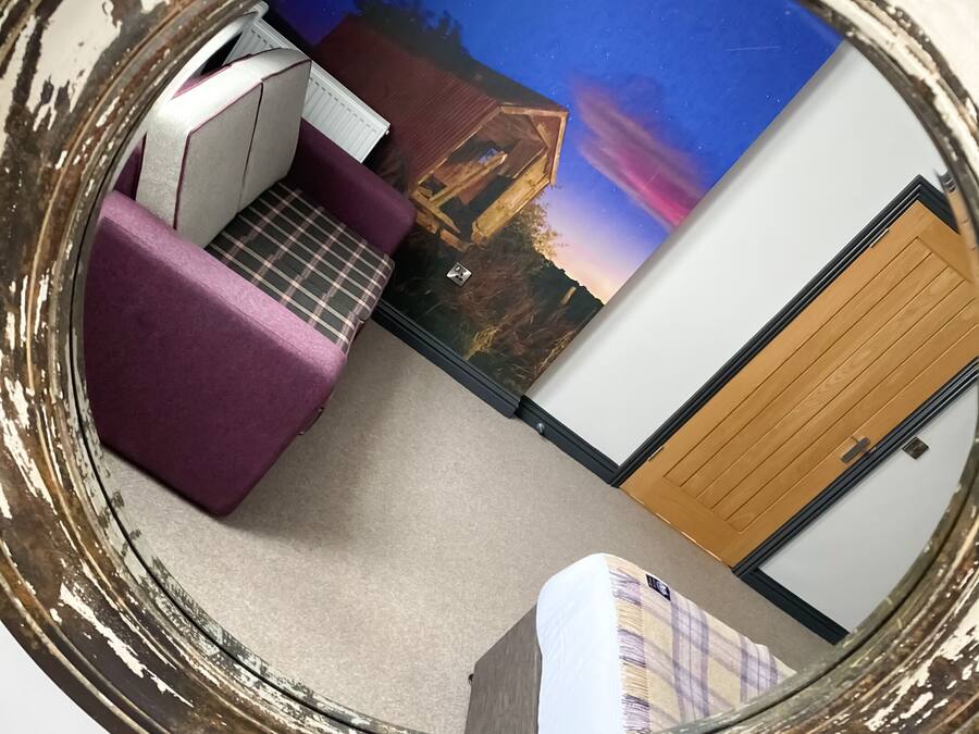 A miniature model of a room with a bed, a desk, and a chair, along with a painting of a sunset over a house.