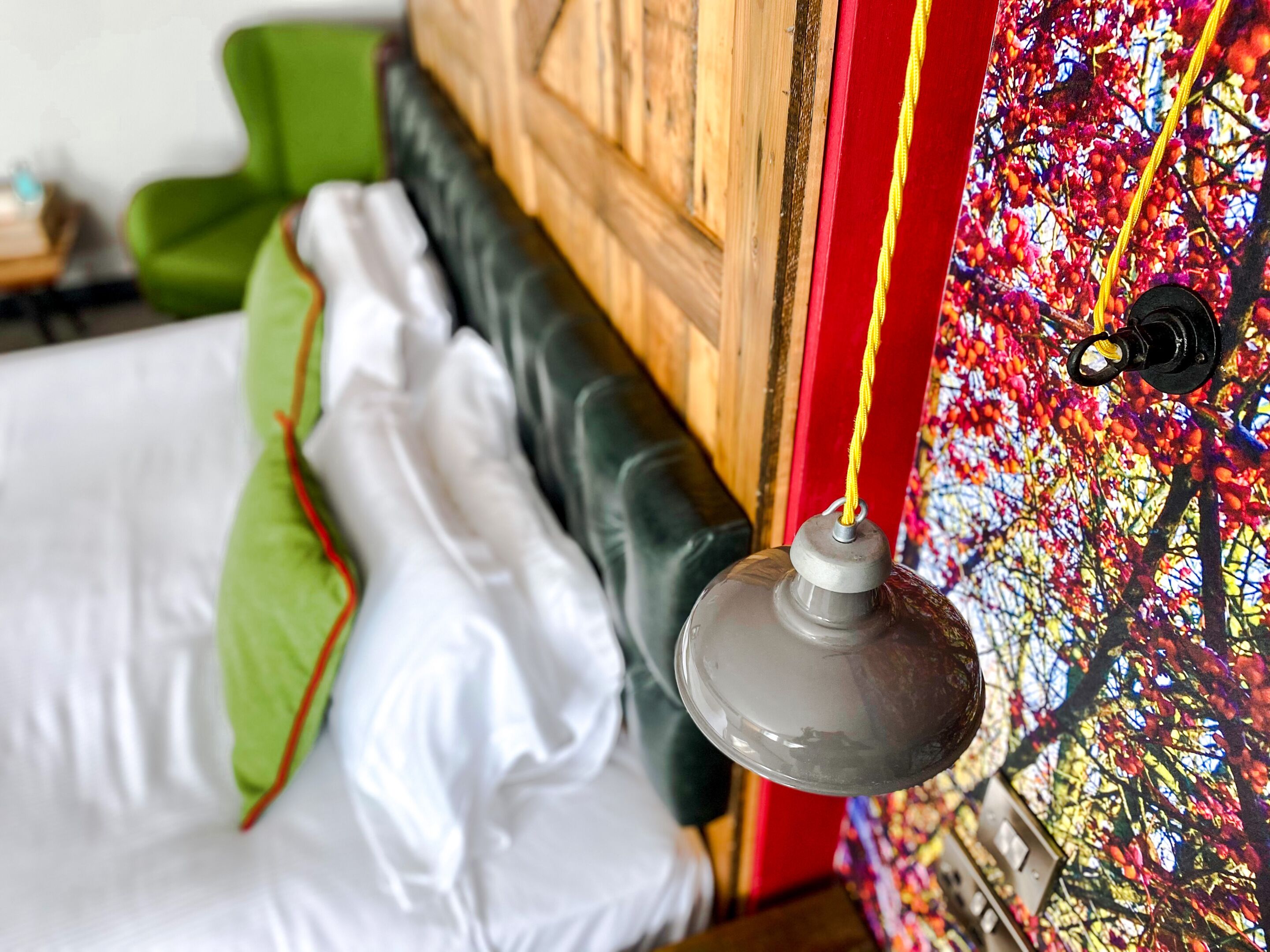 Un letto con biancheria bianca e verde, una testiera in legno e una parete colorata con una finestra.