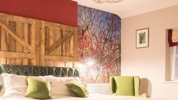 A bedroom with a bed, a wooden headboard, a green chair, and a wall with a tree mural.