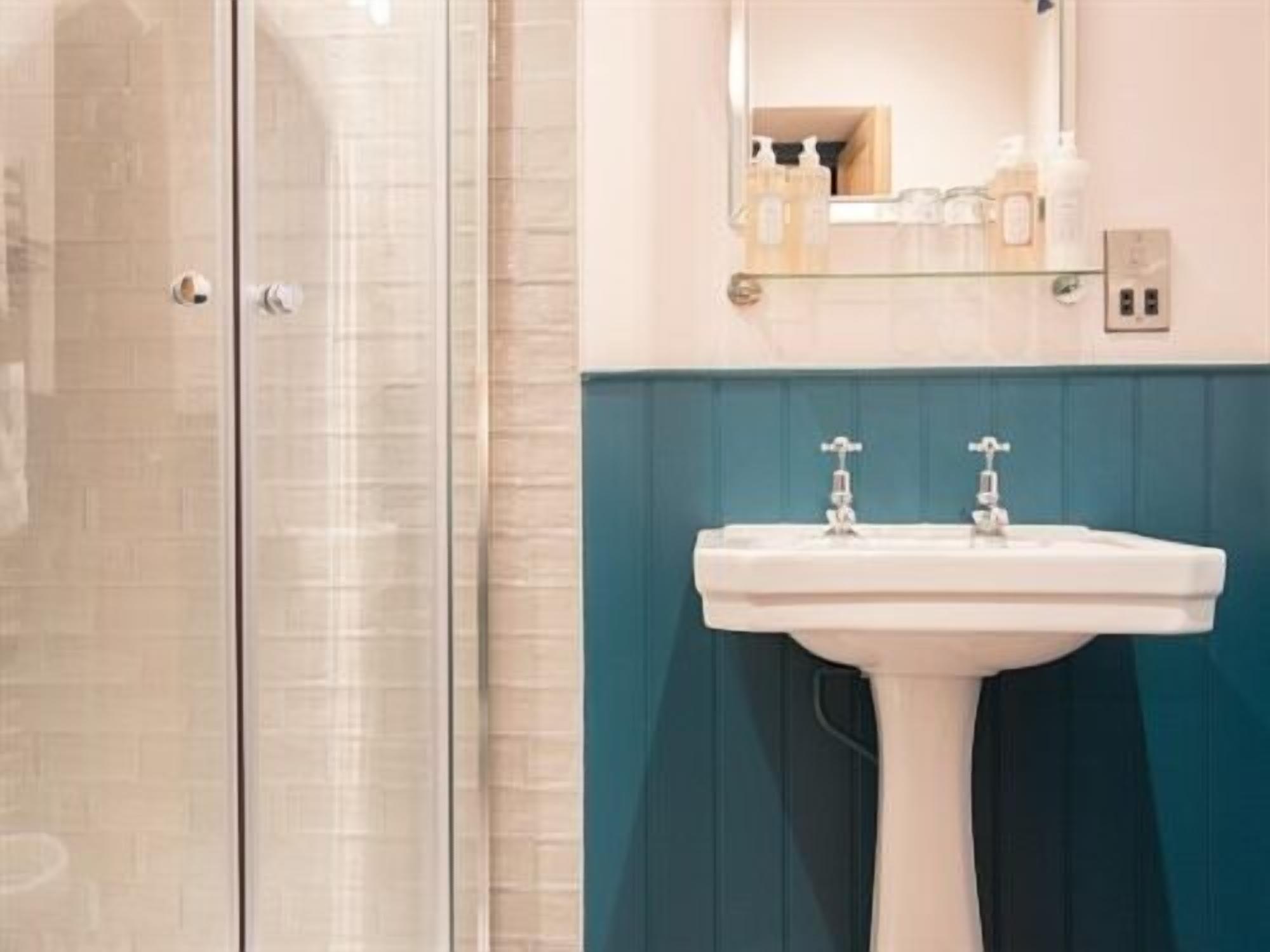 A bathroom with a glass shower enclosure, a white sink with two faucets, and a mirror above the sink.