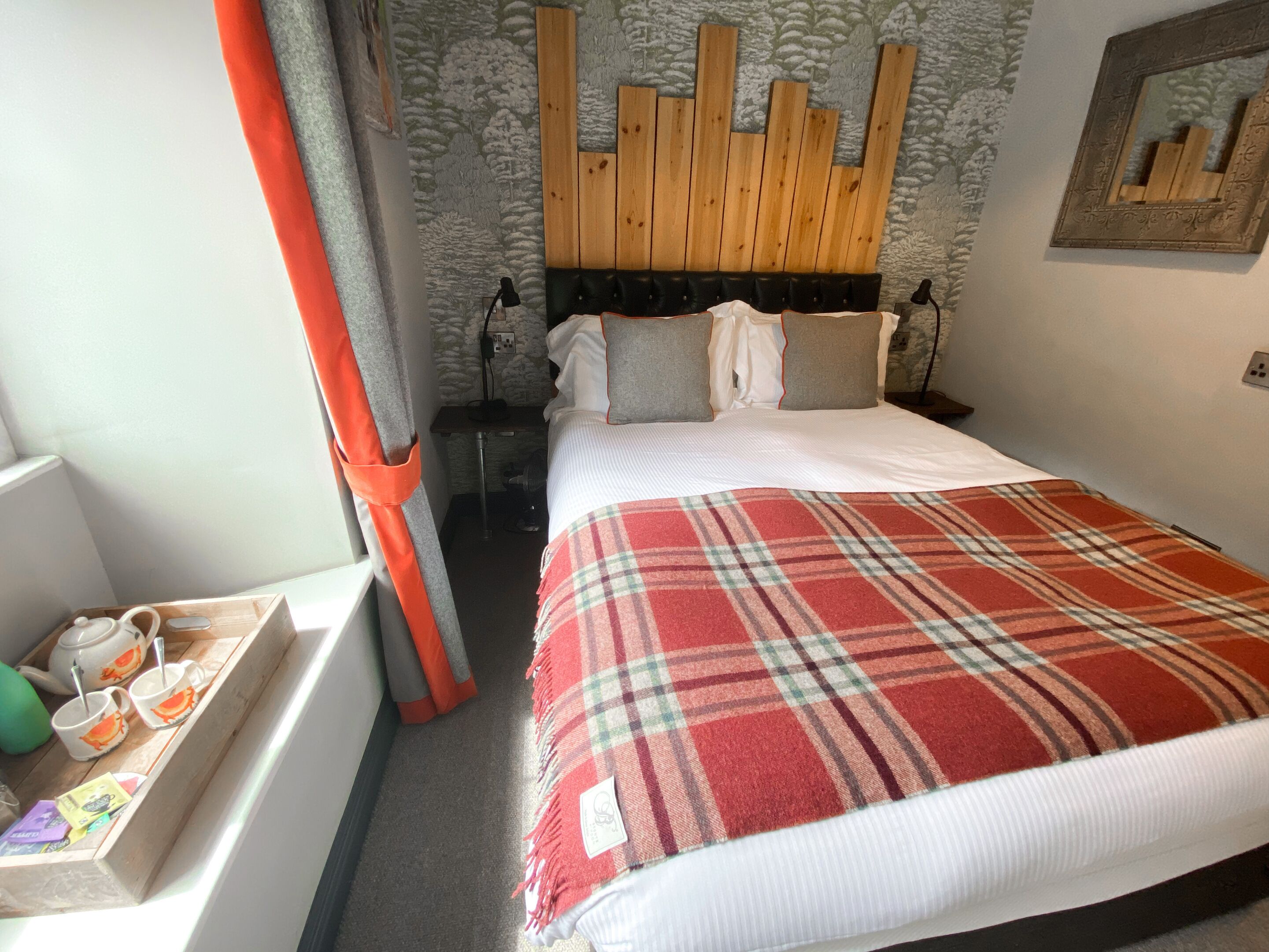 A neatly made bed with a plaid blanket, a wooden headboard, and a small bedside table with a lamp.