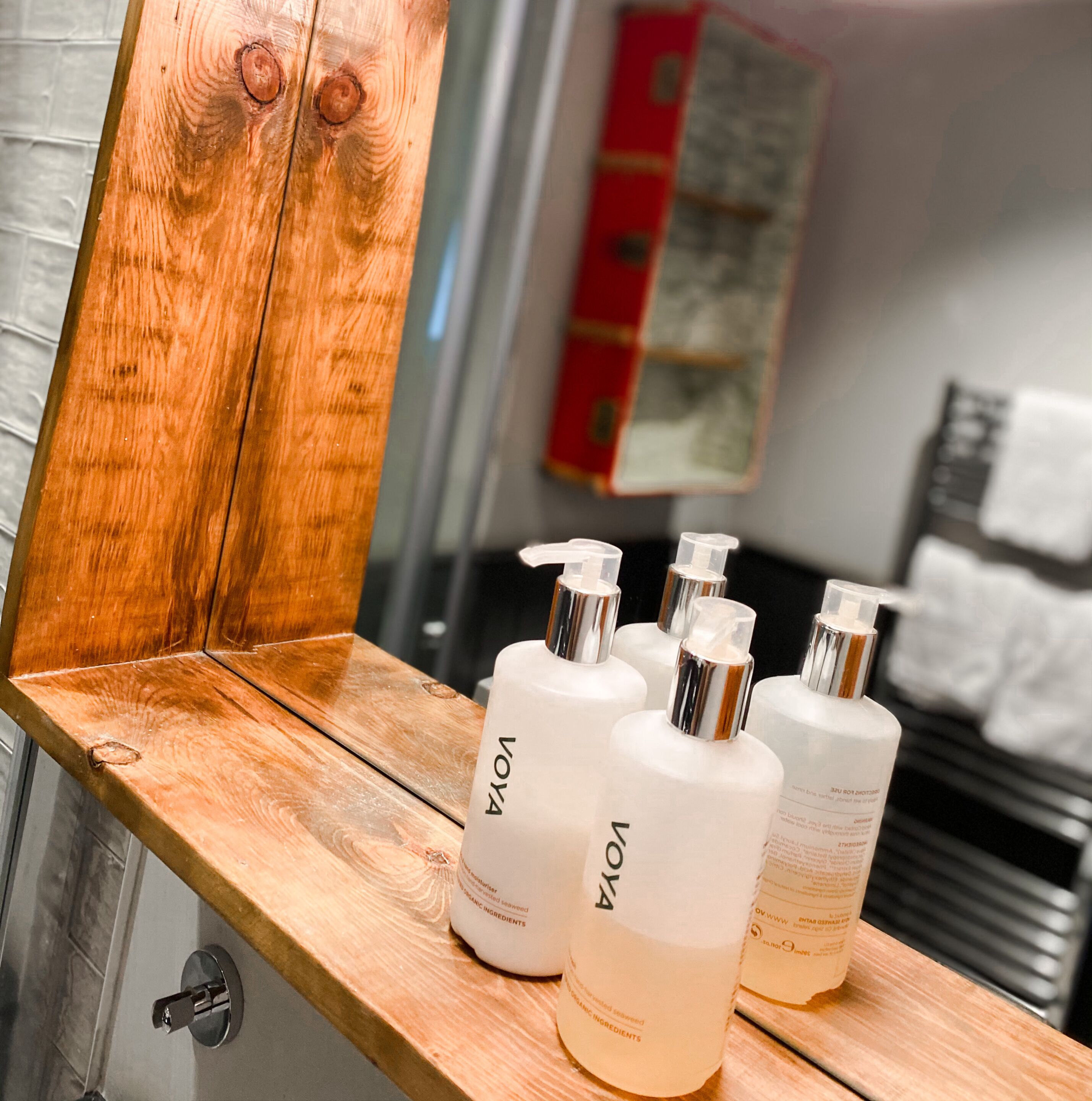 A bathroom vanity with a wooden countertop and a mirror. On the countertop, there are four bottles of Voya body wash.