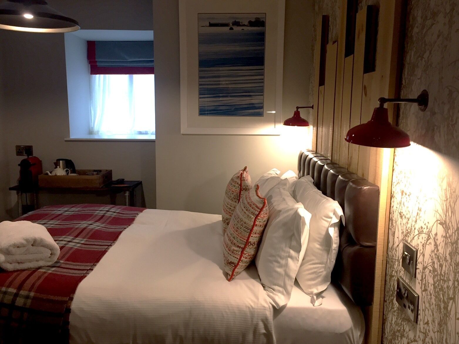 A hotel room with a bed, a desk, a window with curtains, and a wall-mounted heater.