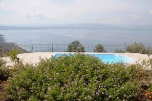 A pool with a view of the sea, surrounded by a fence and greenery.