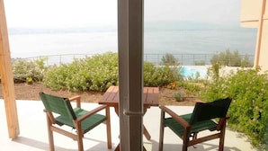 Um pátio com duas cadeiras de madeira e uma mesa, com vista para uma piscina e jardim, e para o mar.