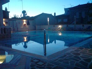 An outdoor swimming pool with a clear water surface, surrounded by stone tiles and a low wall.